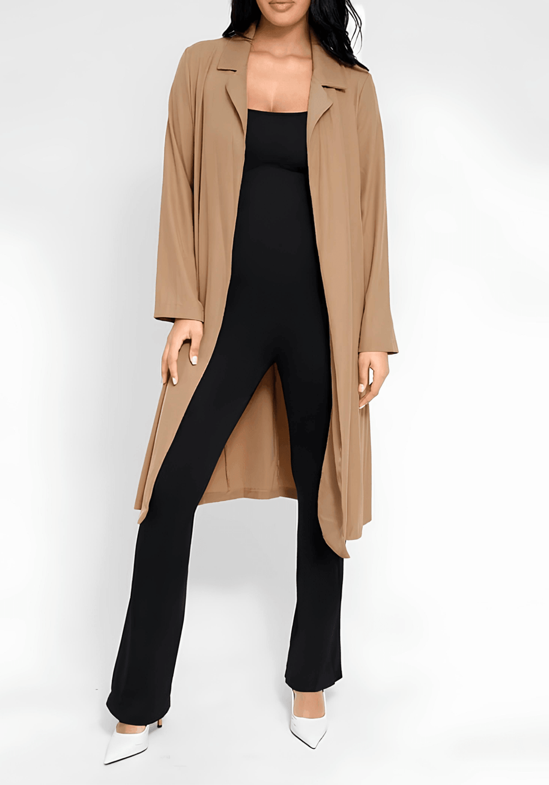 Bodysuit and jumpsuit styling tips: black jumpsuit layered with a tan coat and white heels for a chic look