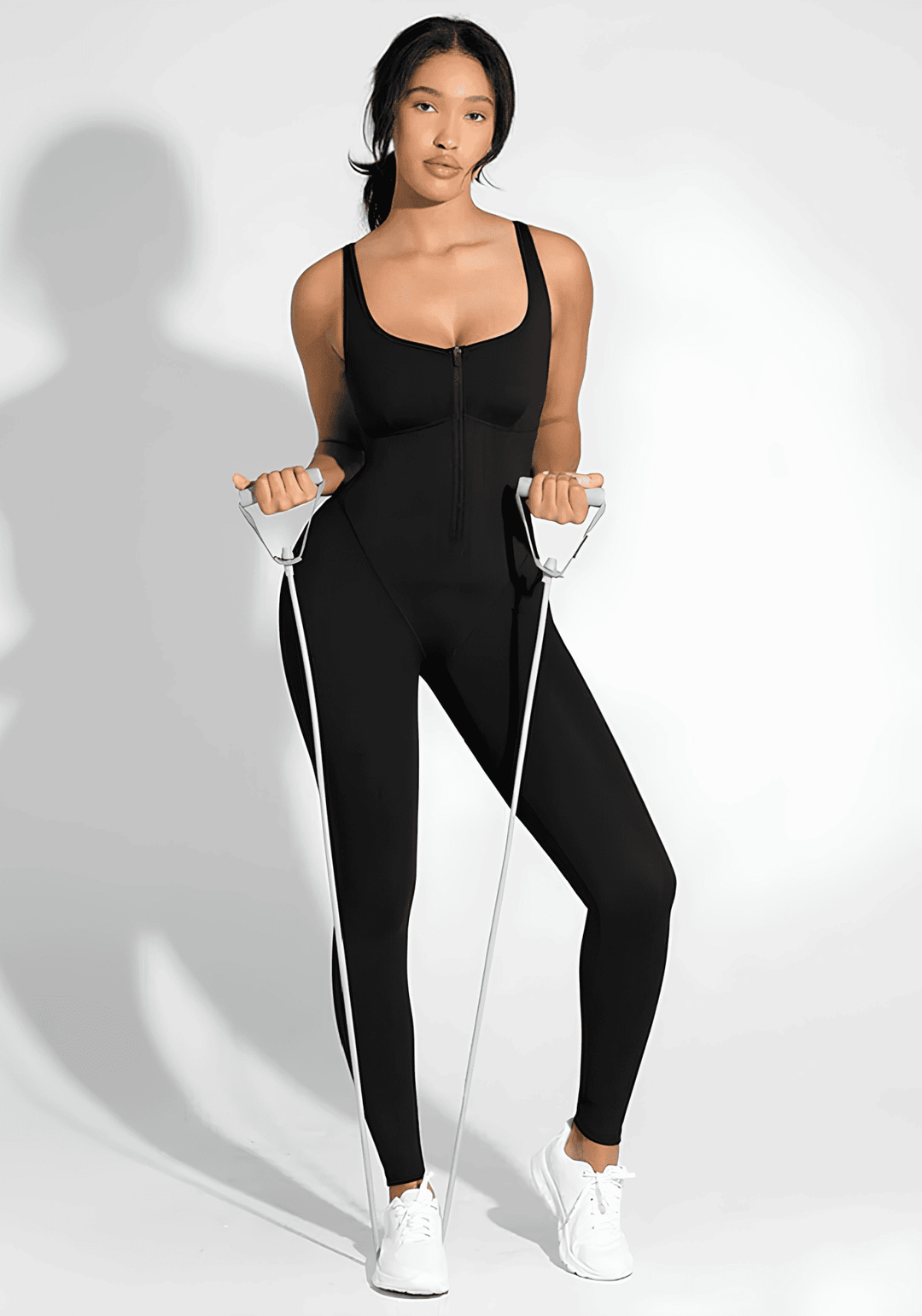 sports sauna jumpsuit styling: woman in black sports sauna jumpsuit with resistance bands and white sneakers
