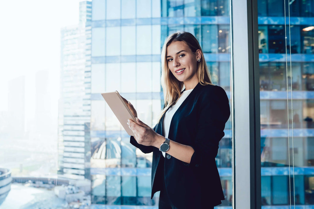 professional shapewear for business women in office attire holding a tablet by a window with city skyline backdrop
