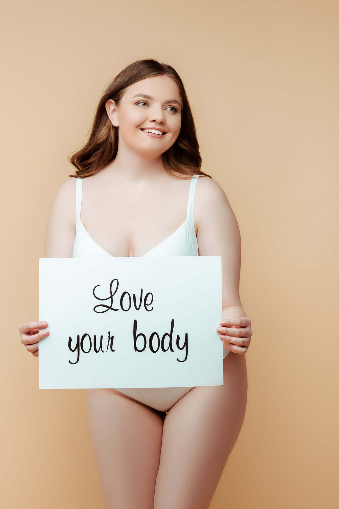 Women’s bodysuits inspiration: smiling woman in white bodysuit holding "Love your body" sign