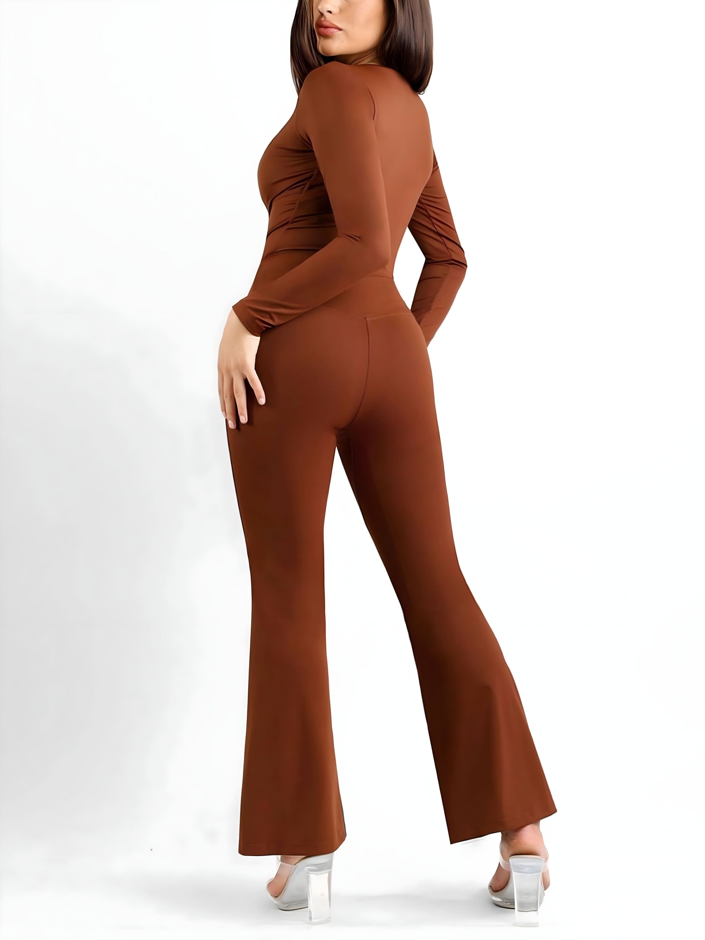 Woman modeling a brown long-sleeve fitted jumpsuit with flared legs and white heels on a white background
