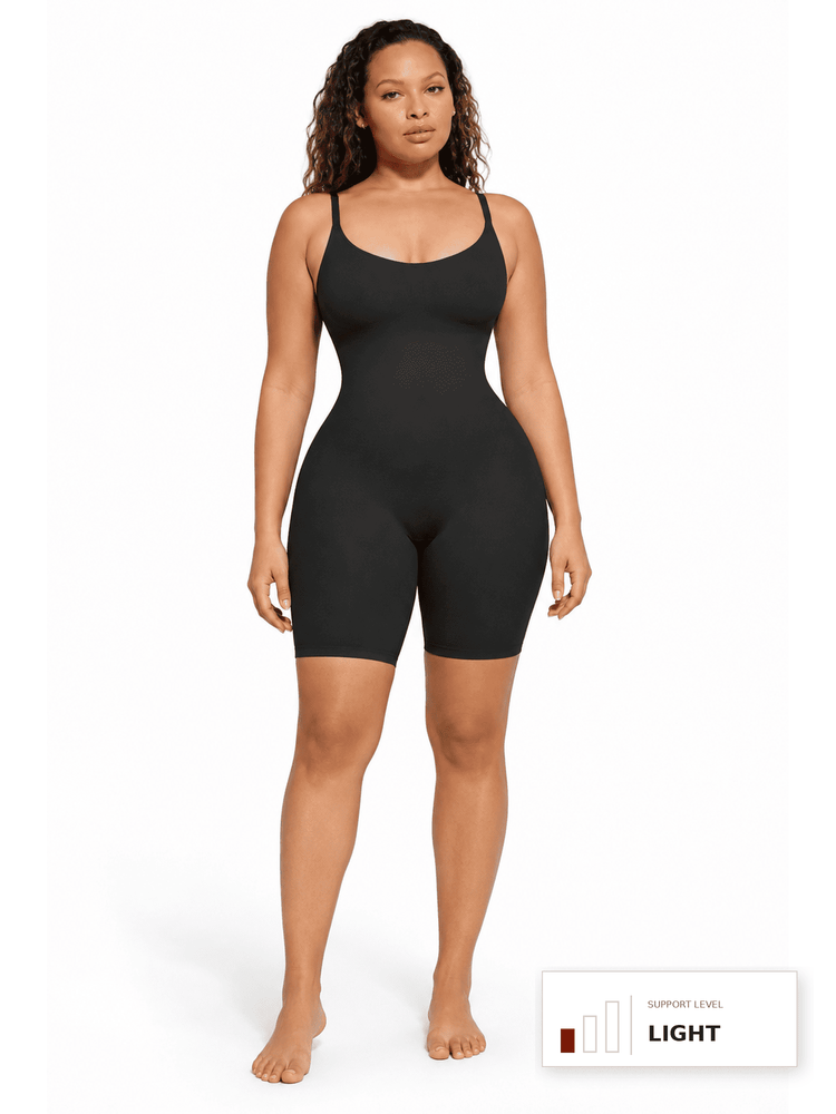 A woman modeling a black bodysuit with shoulder straps and fitted biker shorts against a plain white studio background. A small color indicator label appears in the bottom right corner.