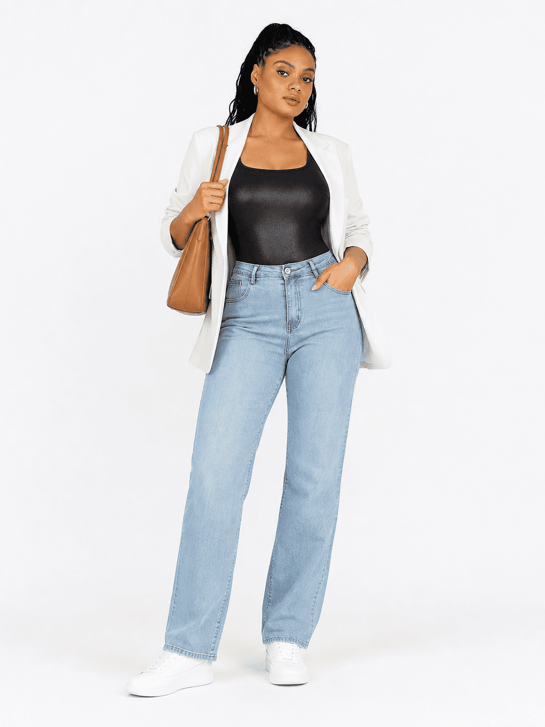 A woman modeling a light wash blue straight-leg denim jeans, styled with a white blazer, black bodysuit, white sneakers, and a brown shoulder bag against a plain white studio background.