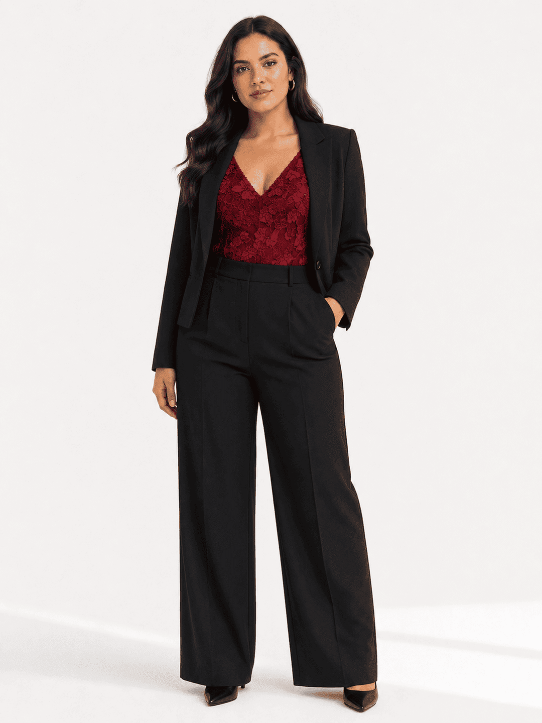 A woman modeling a black wide-leg blazer and matching high-waisted wide-leg trousers, paired with a deep red lace V-neck top, against a plain white studio background.