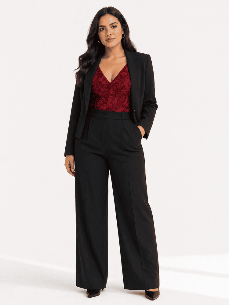 A woman modeling a black wide-leg blazer and matching high-waisted wide-leg trousers, paired with a deep red lace V-neck top, against a plain white studio background.