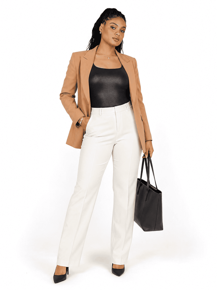 A woman modeling a tan blazer, black faux-leather top, white trousers, and black heels, holding a black tote bag against a plain white background.
