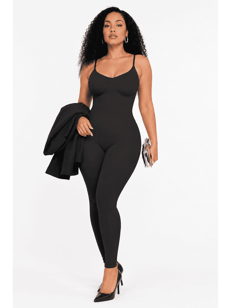 A woman modeling a black bodysuit with thin spaghetti straps and a scoop neckline, styled with a black blazer draped over one arm, a silver clutch, and black pointed-toe heels against a plain white studio background.