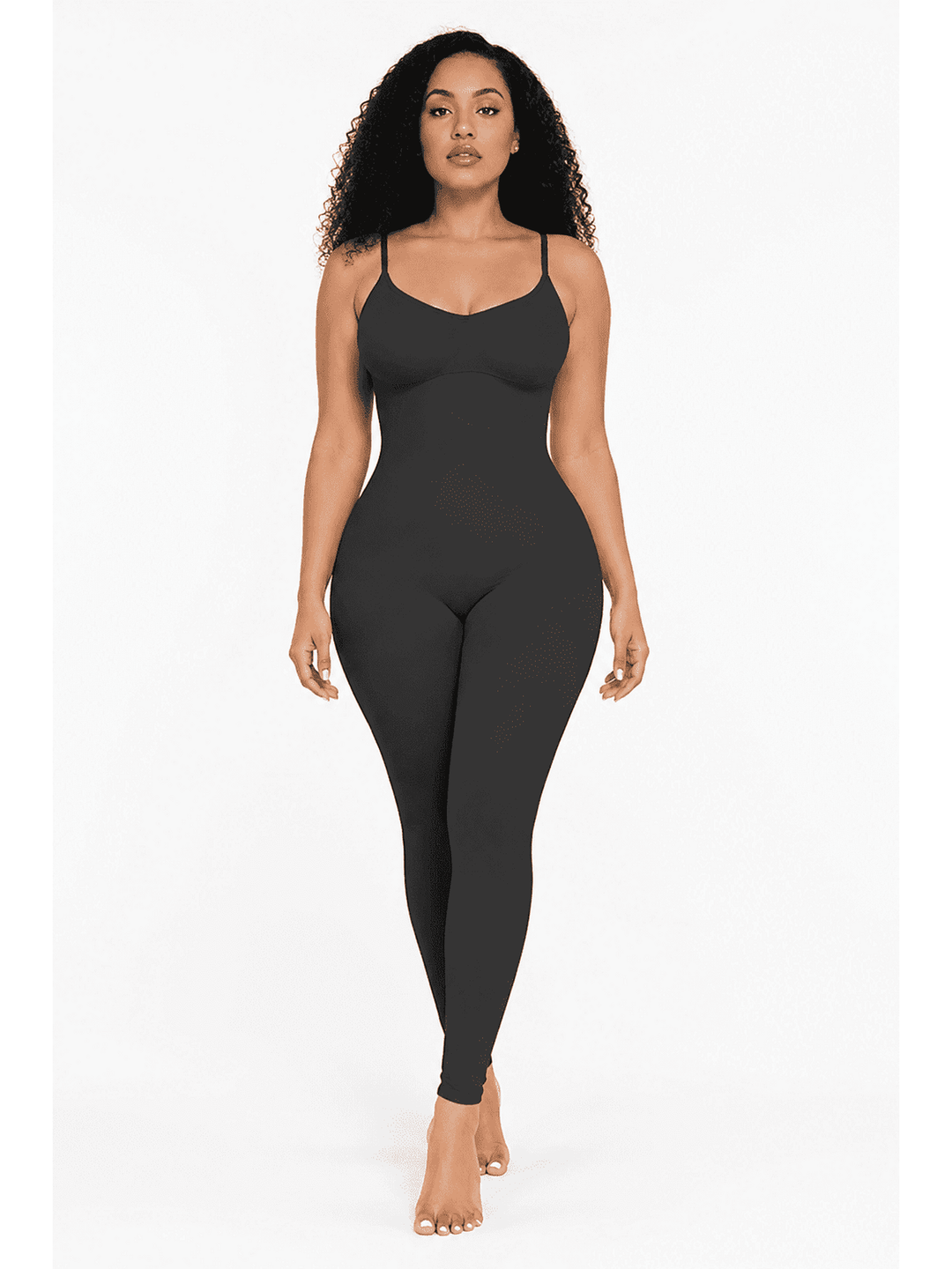 A woman modeling a black shapewear bodysuit with spaghetti straps and a scoop neckline, shown against a plain white studio background.