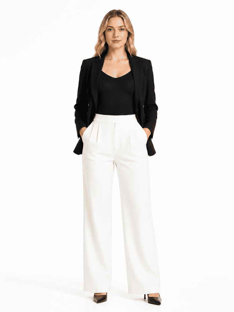 A woman modeling a black blazer over a black top and white wide-leg trousers, standing against a plain white studio background.