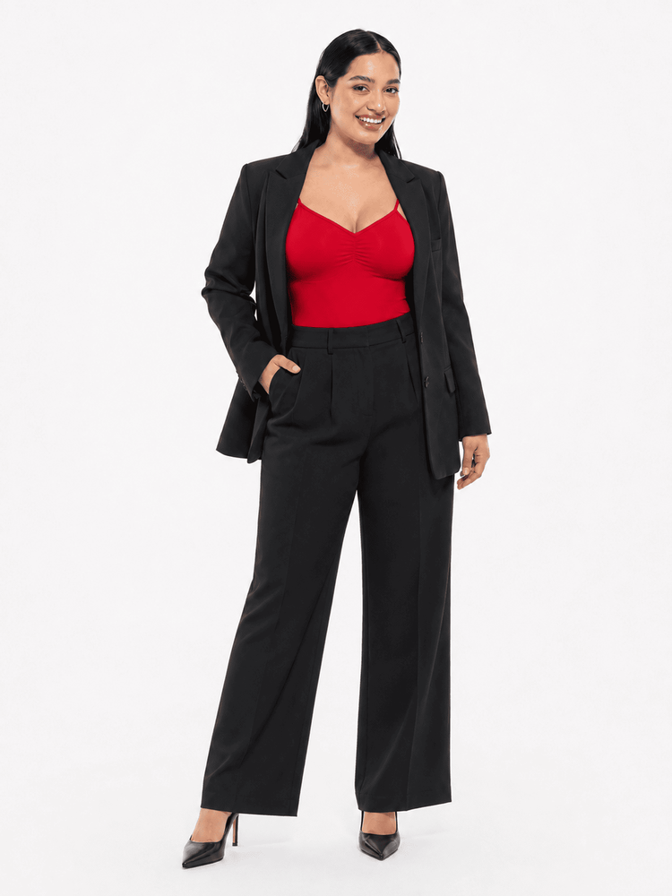 A woman modeling a black wide-leg blazer and matching high-waisted trousers, styled with a bright red sweetheart-neck bodysuit and black pointed-toe heels, against a plain white studio background.