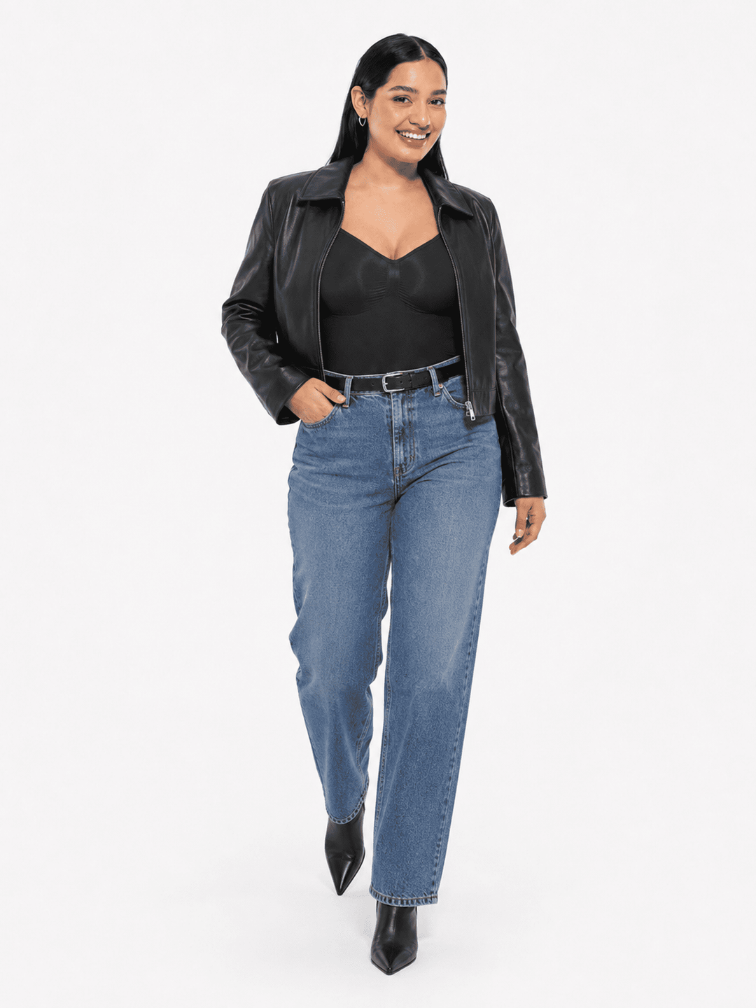 A woman modeling a black leather jacket, black top, and blue jeans against a plain white studio background.