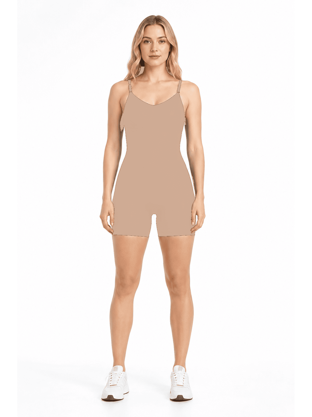 A woman modeling a sleeveless, short-body beige romper or shapewear unitard with thin shoulder straps, paired with white sneakers, against a plain white studio background.