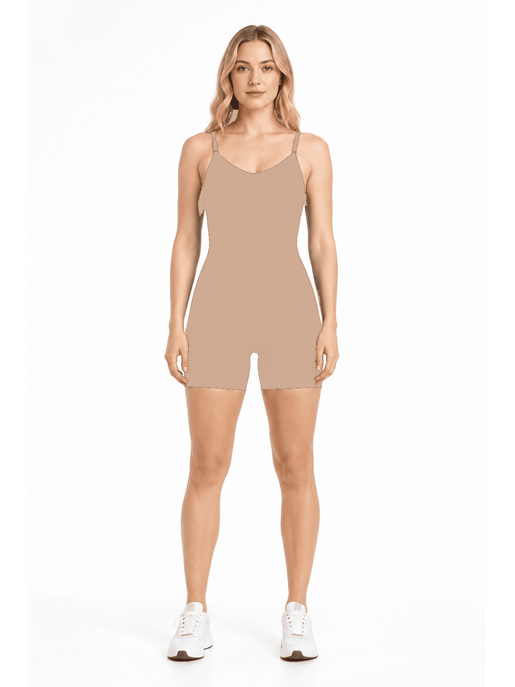 A woman modeling a sleeveless, short-body beige romper or shapewear unitard with thin shoulder straps, paired with white sneakers, against a plain white studio background.