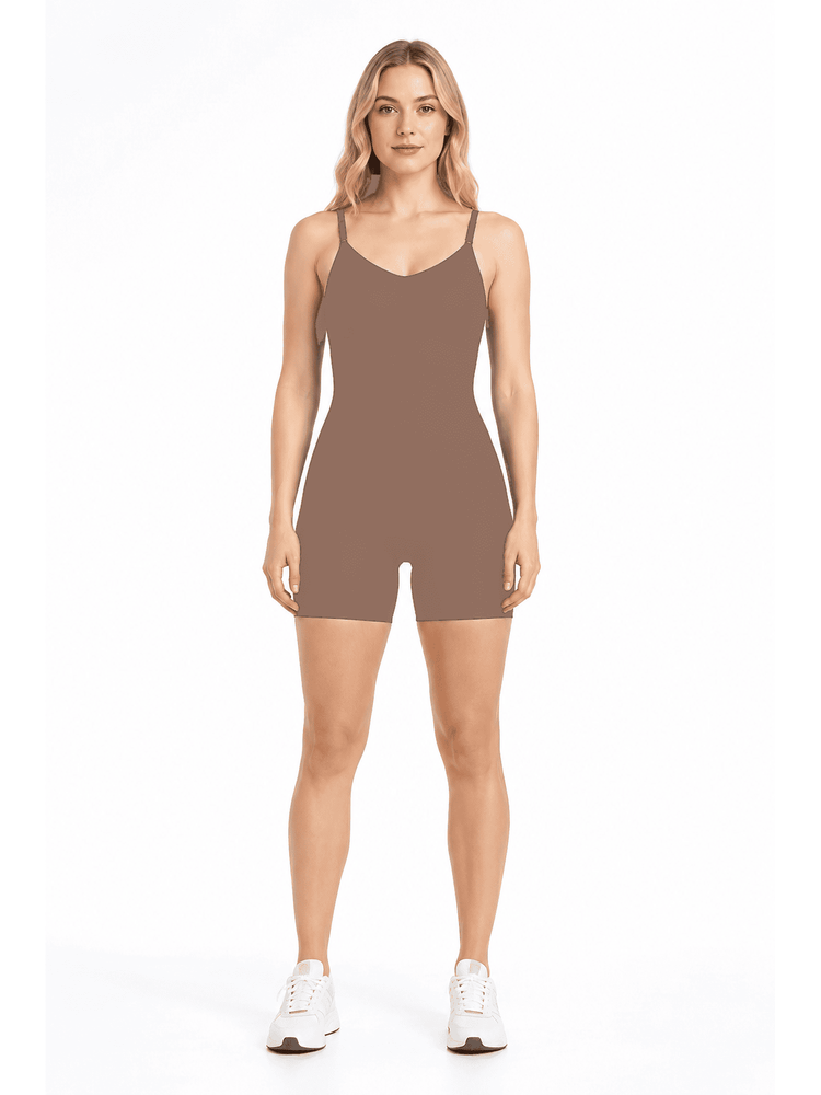 A woman modeling a sleeveless, short-biased athletic romper in a solid taupe-brown color, paired with white sneakers, against a plain white studio background.