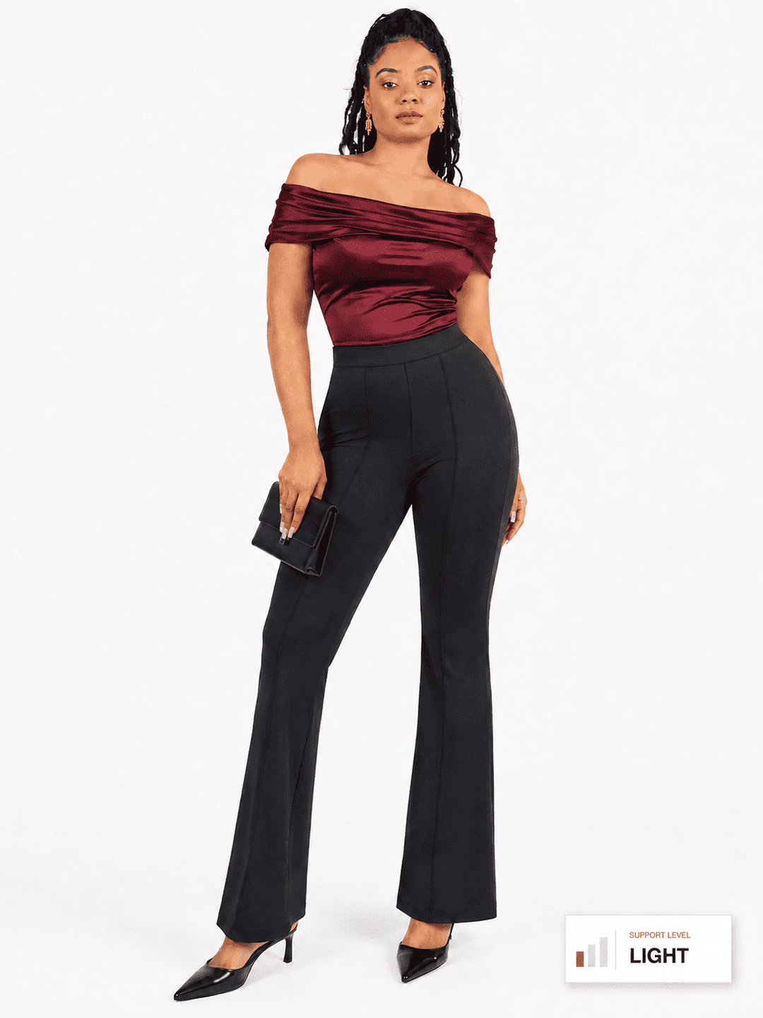 A woman modeling an off-the-shoulder dark burgundy satin top and black high-waisted flared trousers, holding a small black clutch against a plain white studio background.