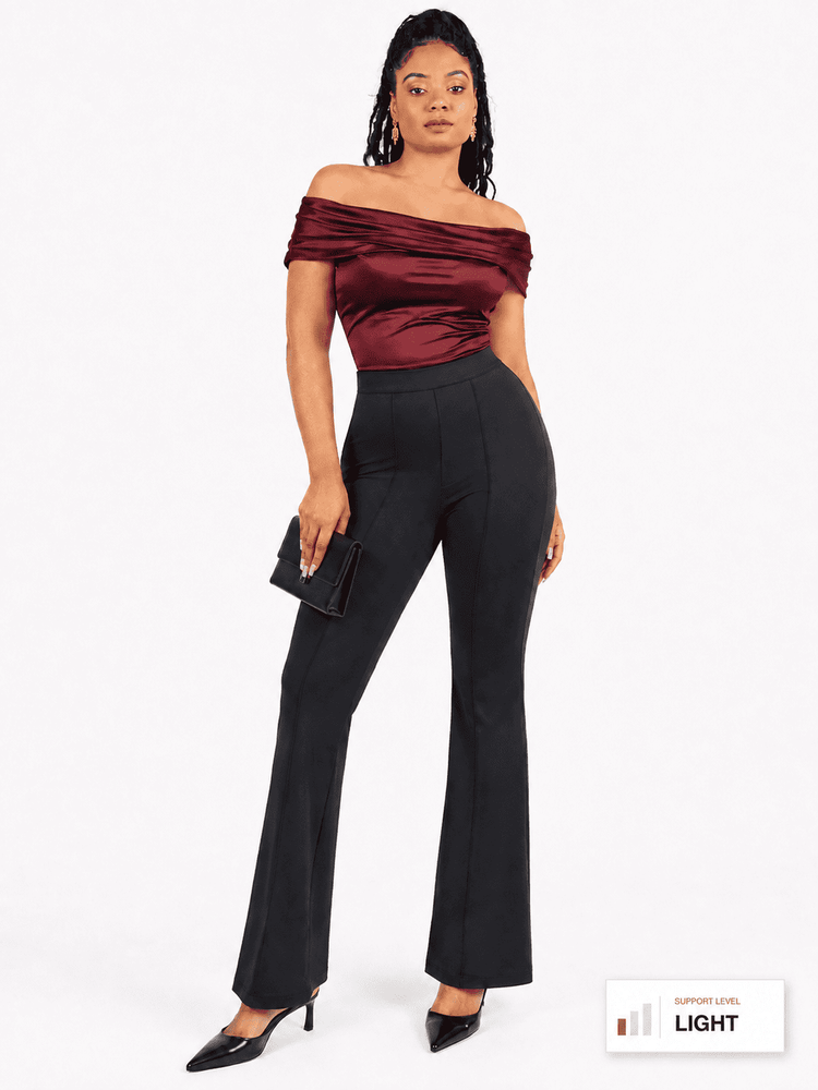 A woman modeling an off-the-shoulder dark burgundy satin top and black high-waisted flared trousers, holding a small black clutch against a plain white studio background.