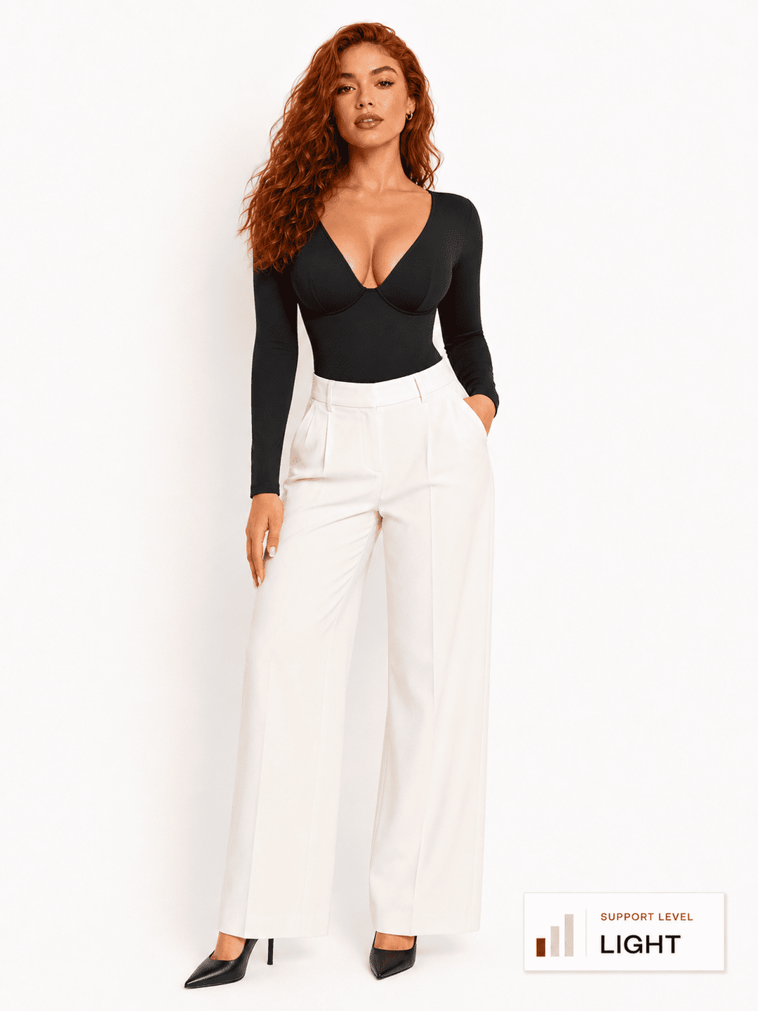 Model wearing a deep V-neck bodysuit with long sleeves paired with white pants.