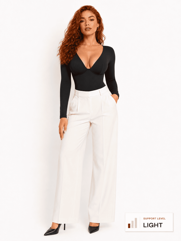 Model wearing a deep V-neck bodysuit with long sleeves paired with white pants.