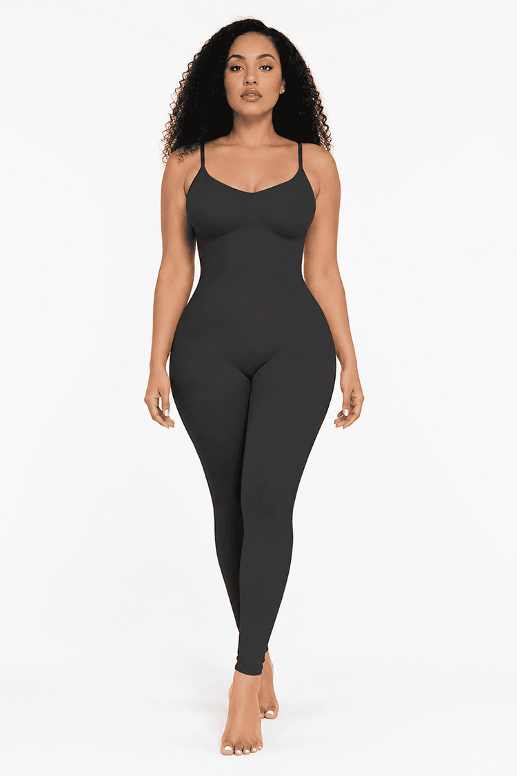 A woman modeling a dark charcoal gray shapewear bodysuit with thin spaghetti straps and a midriff cutout, set against a plain white studio background.