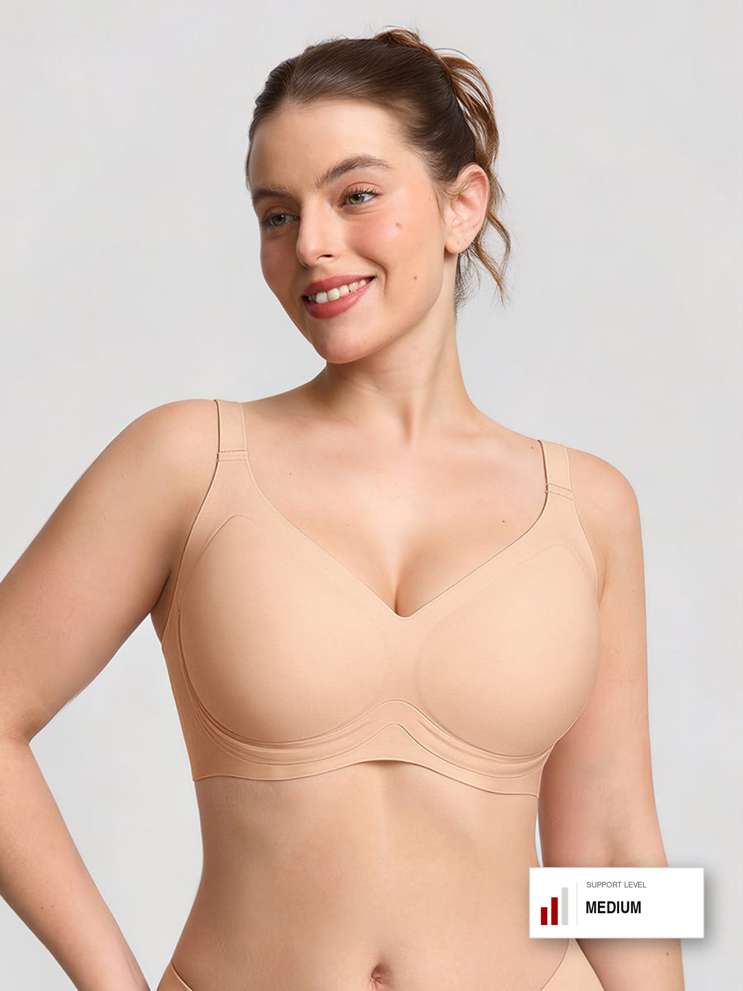 A woman modeling a seamless, medium-cup supportive bra in a light beige/nude color, shown against a light gray studio background with a 'SUPPORT LEVEL MEDIUM' badge in the bottom right corner.