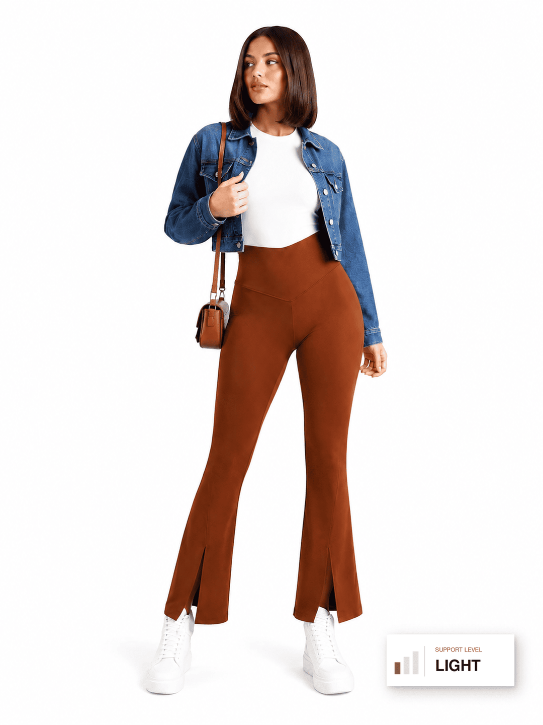 A woman modeling high-waisted, rust-brown flared pants with front slits, styled with a white top, blue denim jacket, white sneakers, and a small brown shoulder bag against a plain white background.