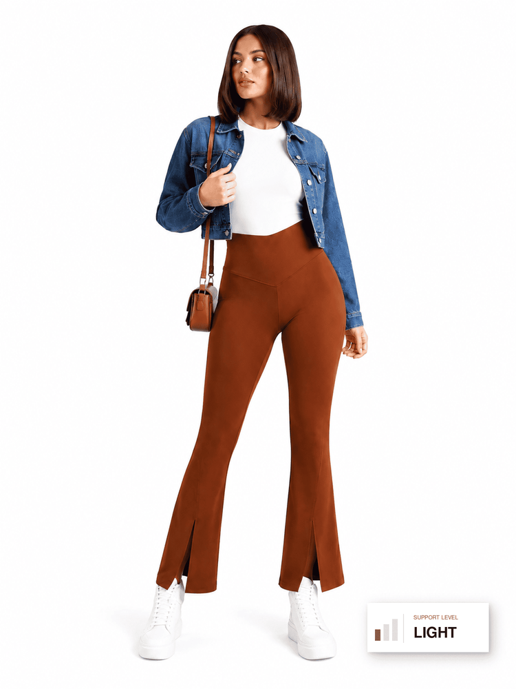 A woman modeling high-waisted, rust-brown flared pants with front slits, styled with a white top, blue denim jacket, white sneakers, and a small brown shoulder bag against a plain white background.