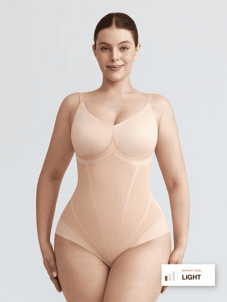 A woman modeling a light beige seamless shapewear bodysuit against a light gray studio background. A small label in the bottom right corner reads 'SUPPORT LEVEL LIGHT'.
