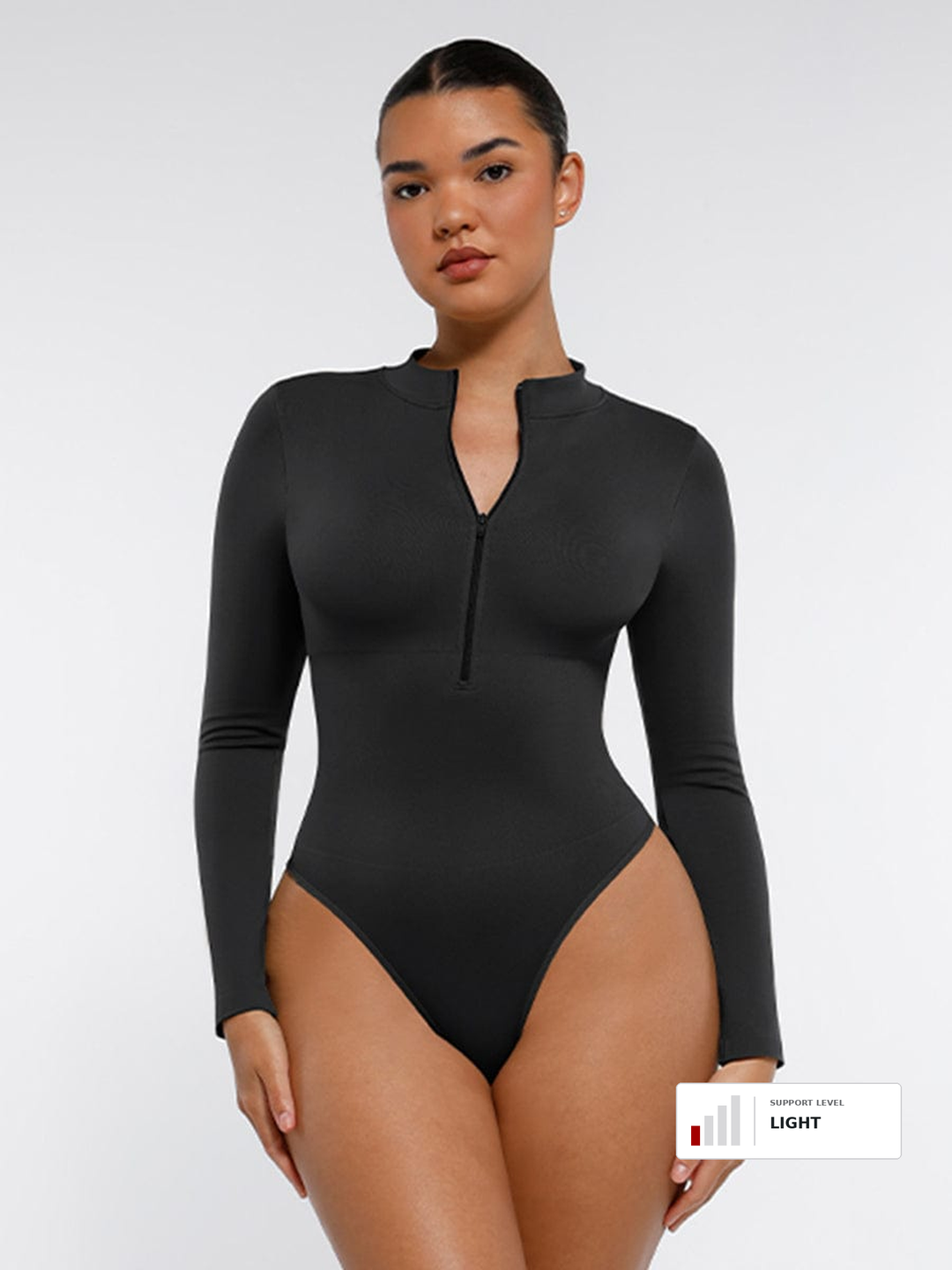 A model wearing a black long-sleeve bodysuit with a half-zip neckline, shown against a light gray studio background. A small color label in the bottom right corner reads 'LIGHT'.