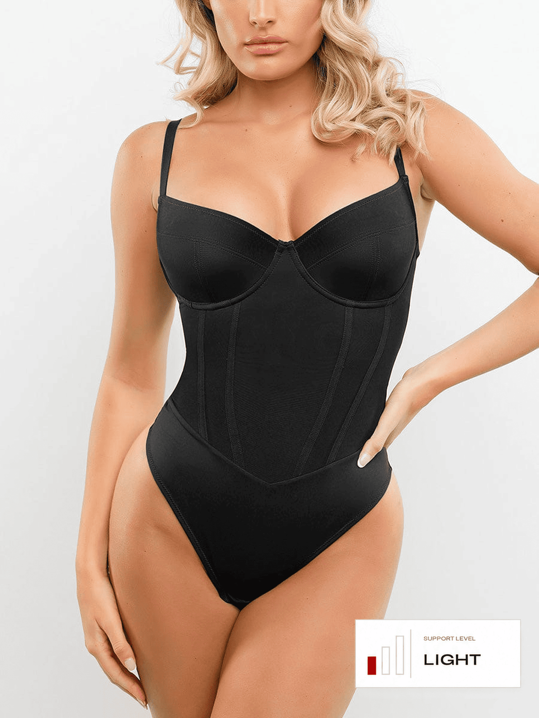 A woman modeling a black structured bodysuit with underwire cups and a corset-style front, shown against a light gray studio background. A small label in the lower right reads 'SUPPORT LEVEL LIGHT'.