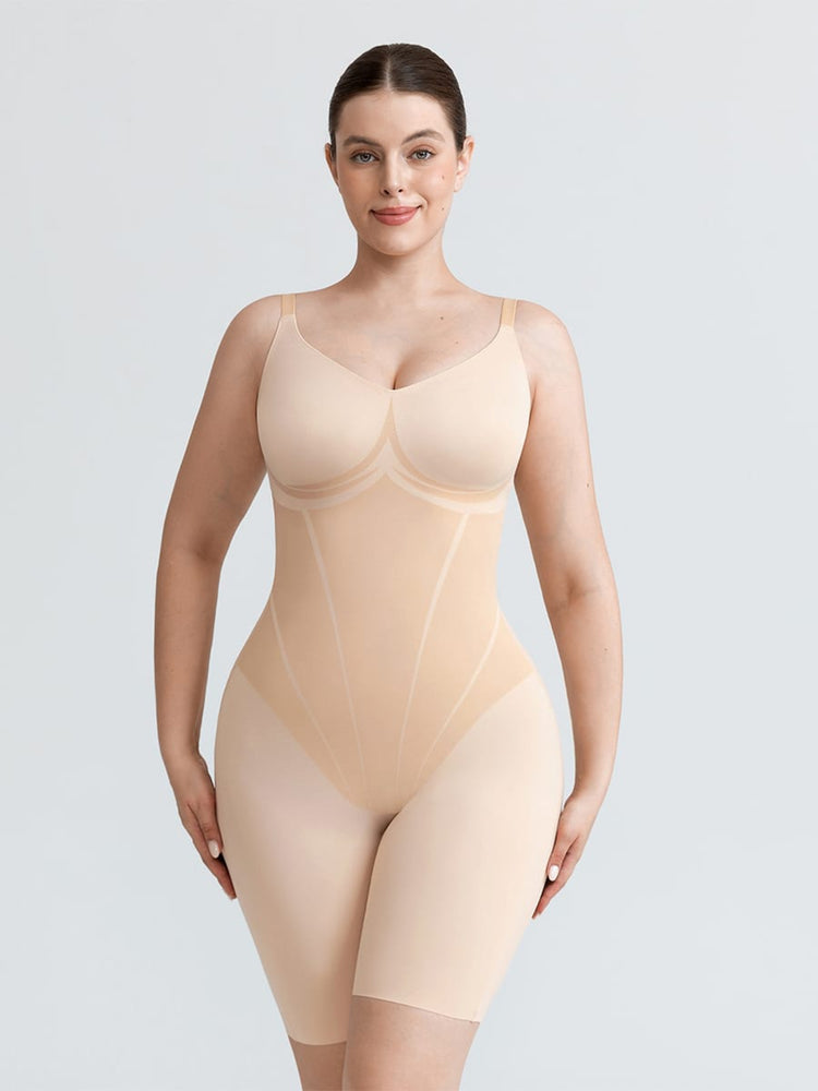 A woman modeling a nude-beige compression bodysuit with built-in bra cups and mid-thigh leggings, shown against a light gray studio background.