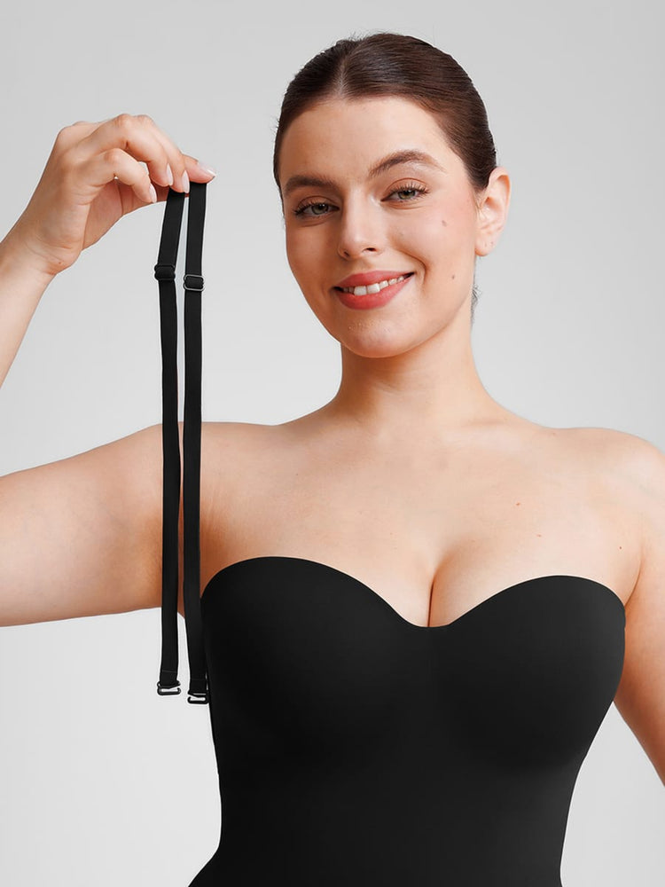 Woman wearing a black strapless garment holding a black strap against a plain background