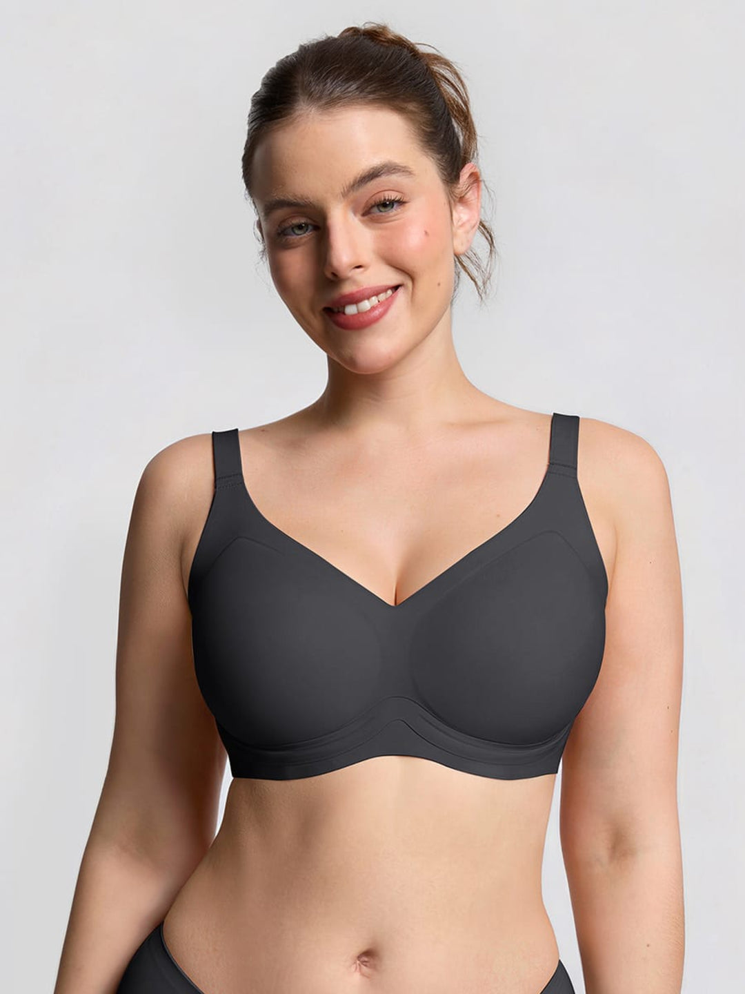 A woman modeling a dark gray wireless bra against a light gray studio background.