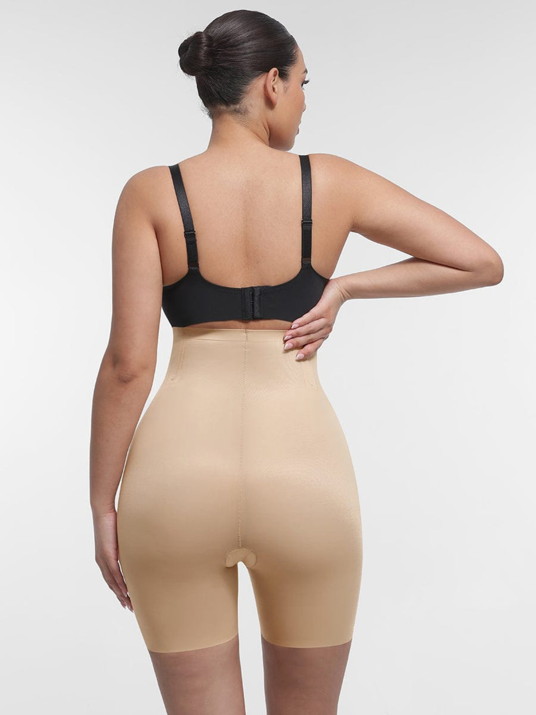 Woman wearing a black bra and beige shapewear on a white background