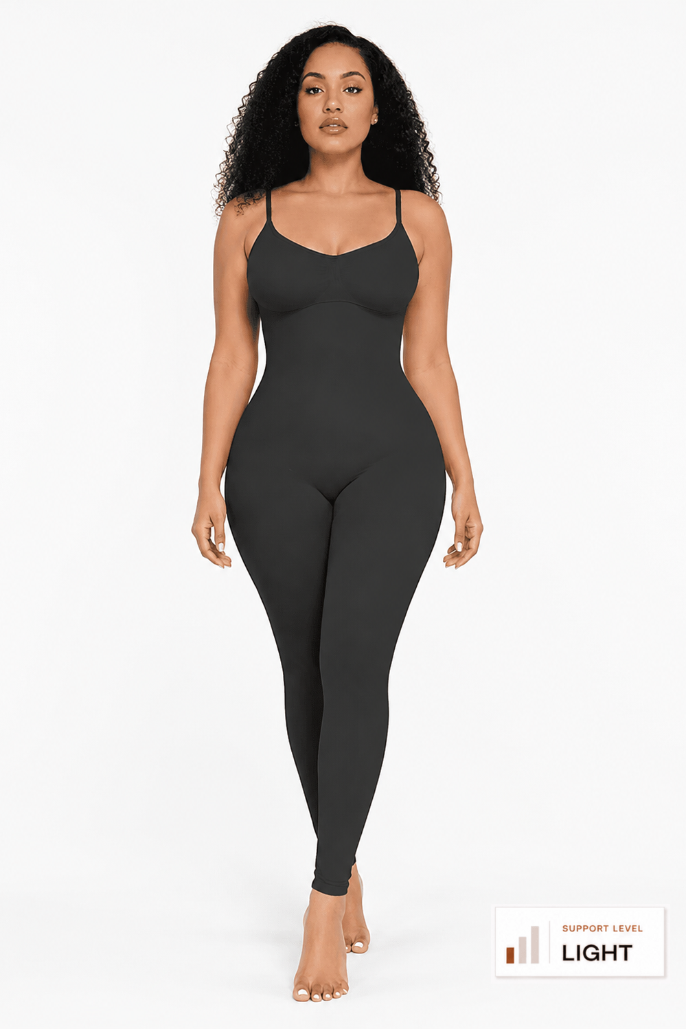 A woman modeling a dark charcoal gray full-body bodysuit or jumpsuit against a plain light gray studio background. The garment has thin shoulder straps, a fitted silhouette, and a scoop neckline.