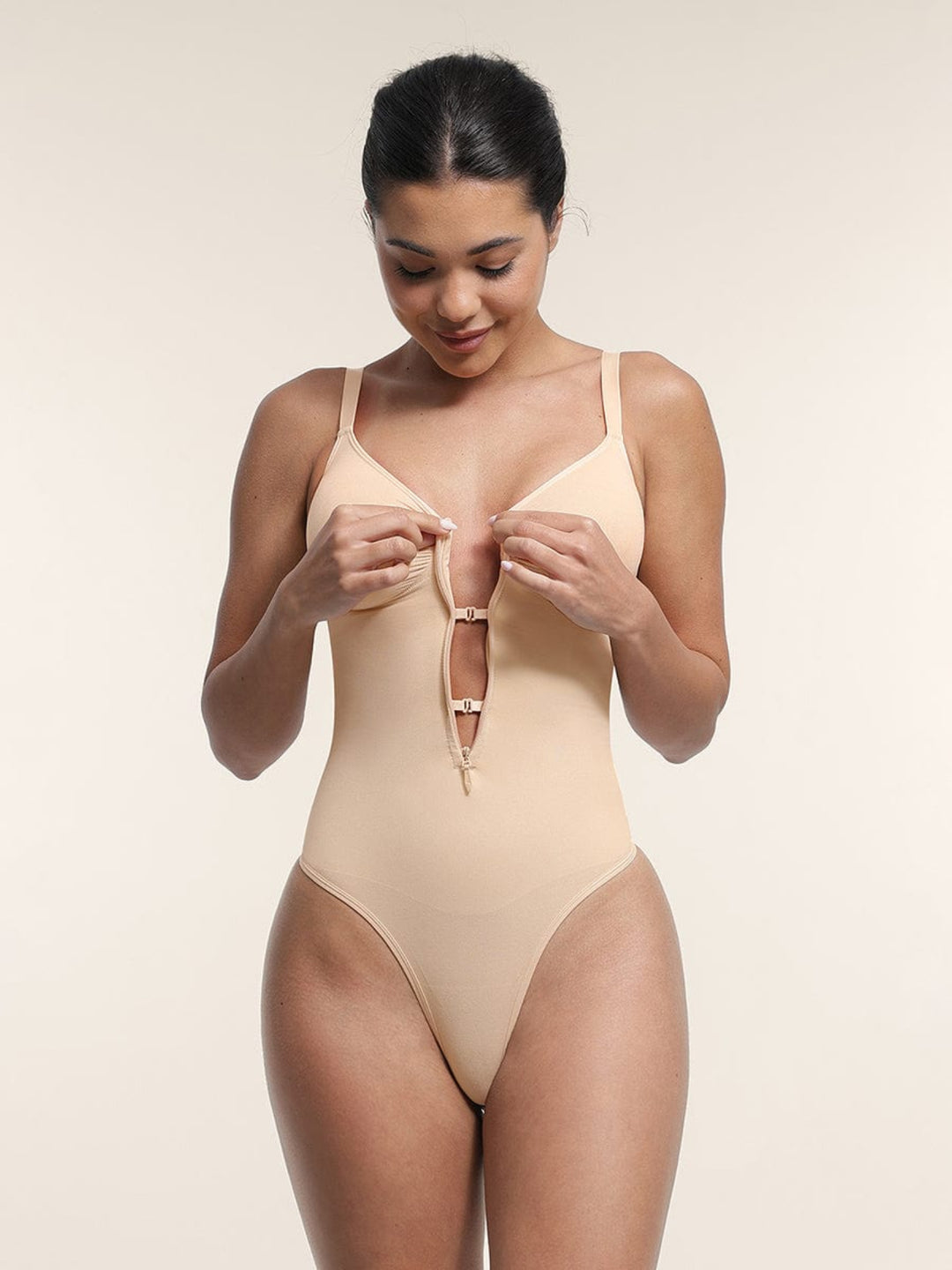 Woman wearing a beige bodysuit against a plain background
