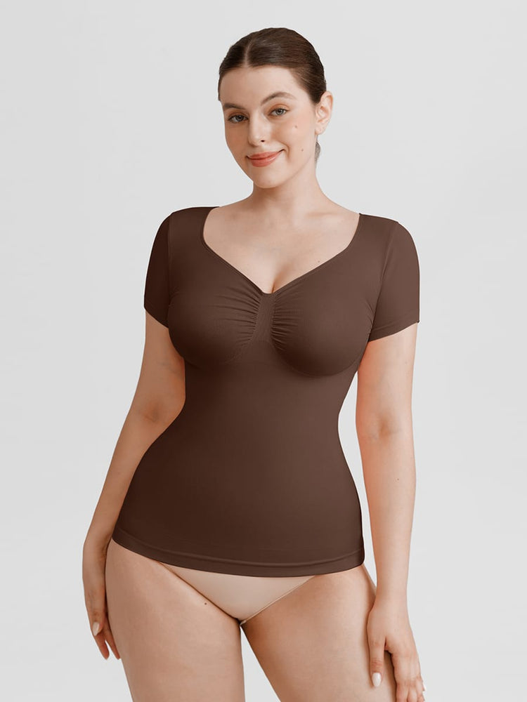 A woman modeling a short-sleeve brown bodysuit with a ruched sweetheart neckline, shown against a plain light gray studio background.
