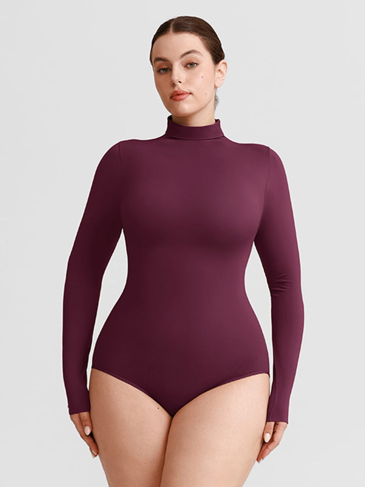 A woman modeling a long-sleeve, high-neck bodysuit in a deep plum purple color, photographed against a solid light gray background.