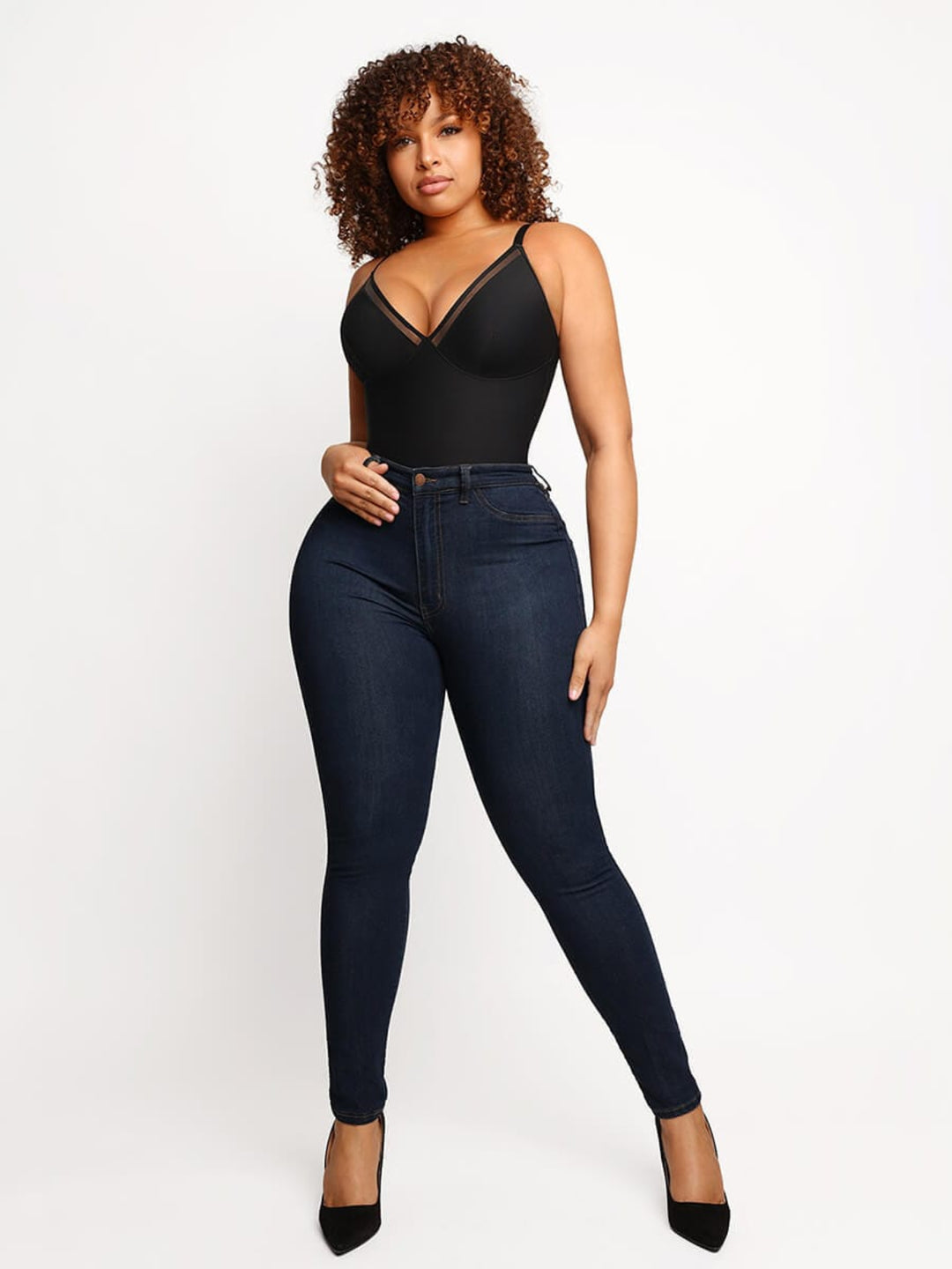 Woman wearing a black bodysuit and dark blue jeans on a white background