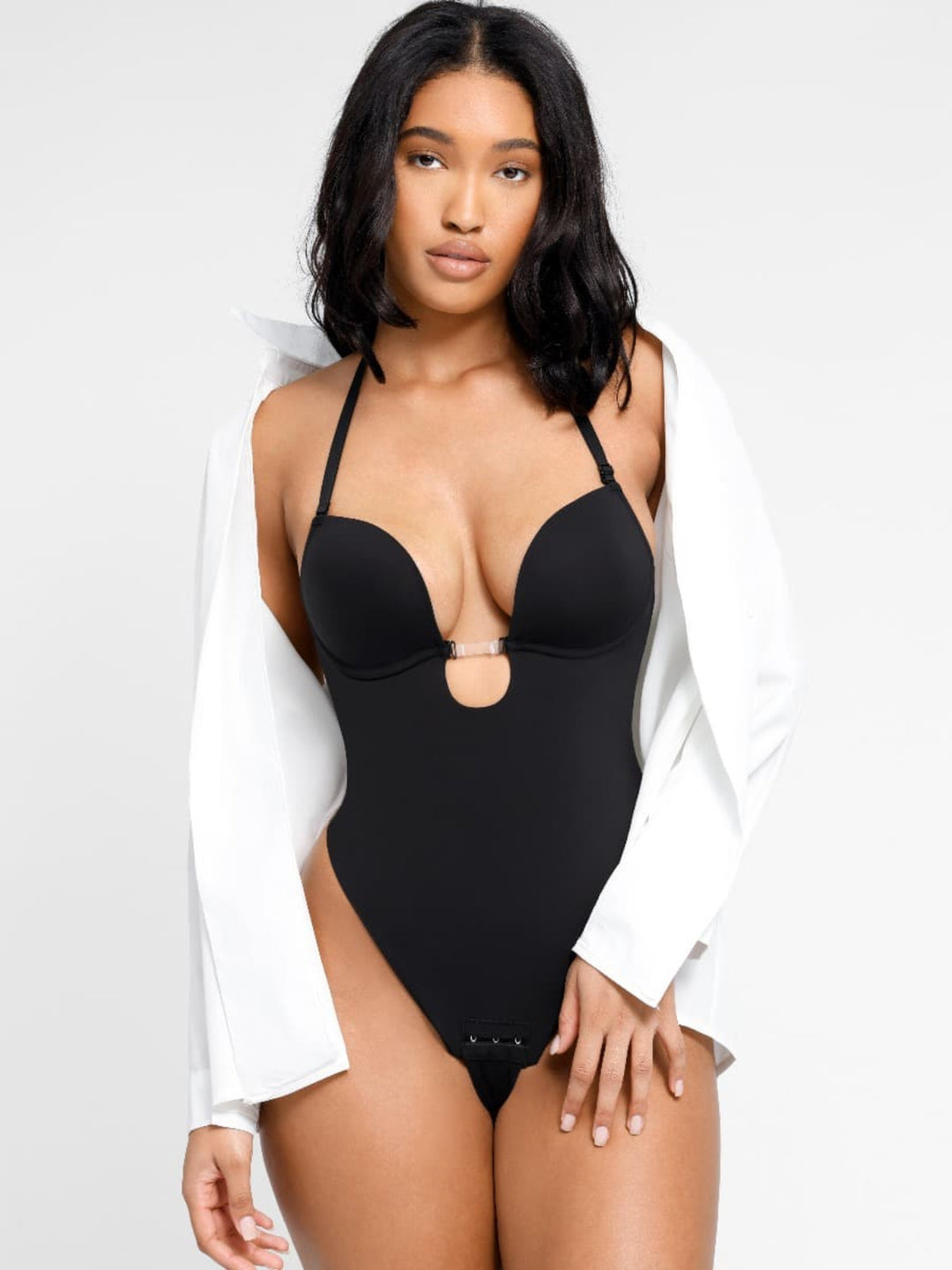 Woman wearing a black swimsuit with a white shirt over her shoulders on a light gray background
