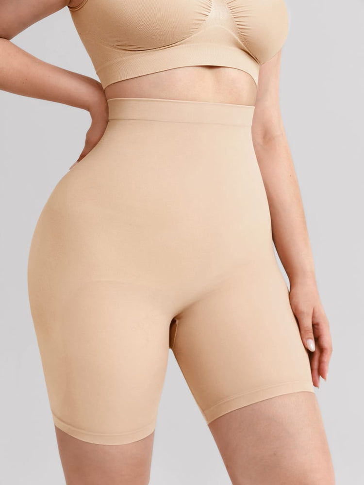 A close-up of a model wearing a beige high-waisted shapewear brief and matching bra against a solid light gray background.