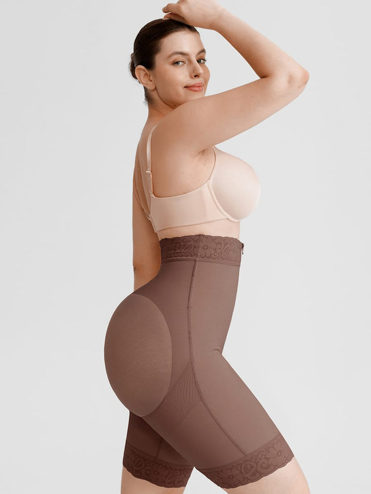 A woman modeling high-waisted brown shapewear briefs with lace trim, paired with a light beige bra, against a solid light gray studio background.