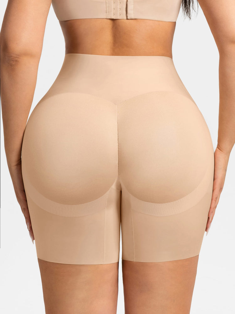 Rear view of a model wearing high-waisted beige shapewear shorts with built-in butt pads, paired with a matching beige sports bra, against a light gray background.