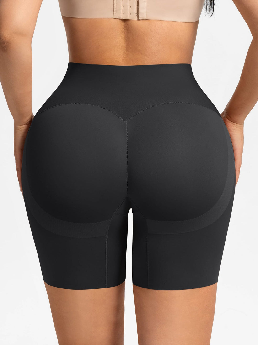 Rear view of a model wearing black high-waisted shapewear biker shorts against a light gray studio background.