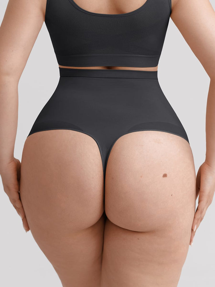 Rear view of a model wearing a black sports bra and high-waisted black briefs against a light gray background.
