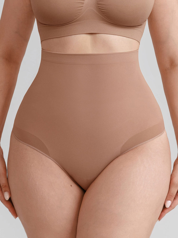 A close-up of a model wearing high-waisted shapewear briefs in a warm nude beige color, paired with matching bra top.