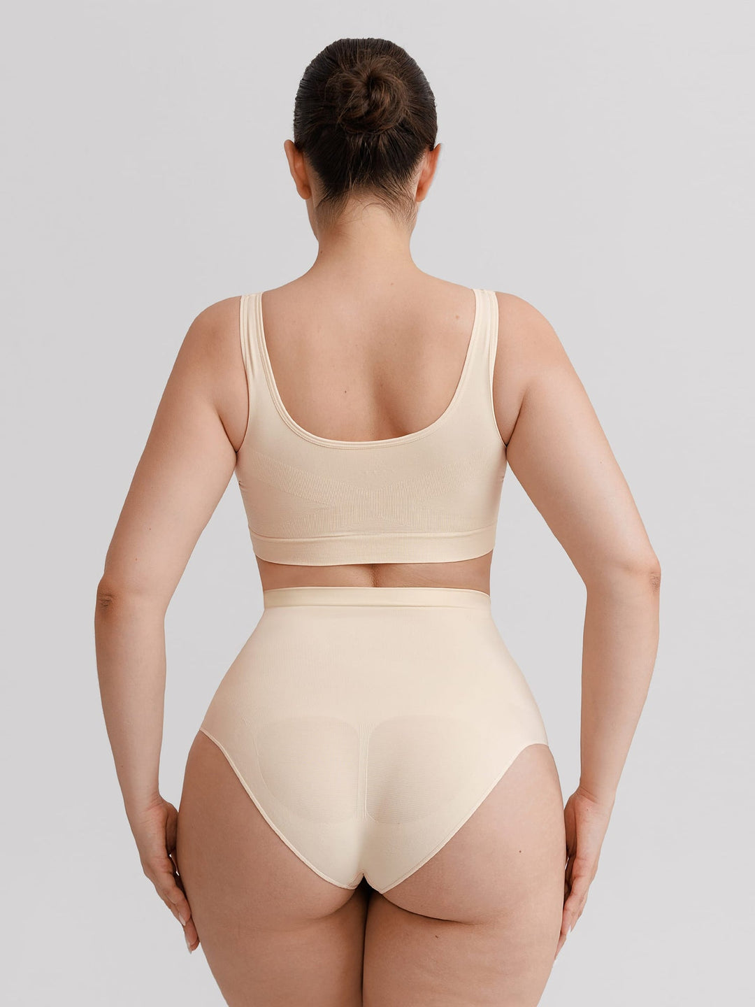 A woman shown from the back wearing a matching beige bralette and high-waisted brief set against a light gray studio background.