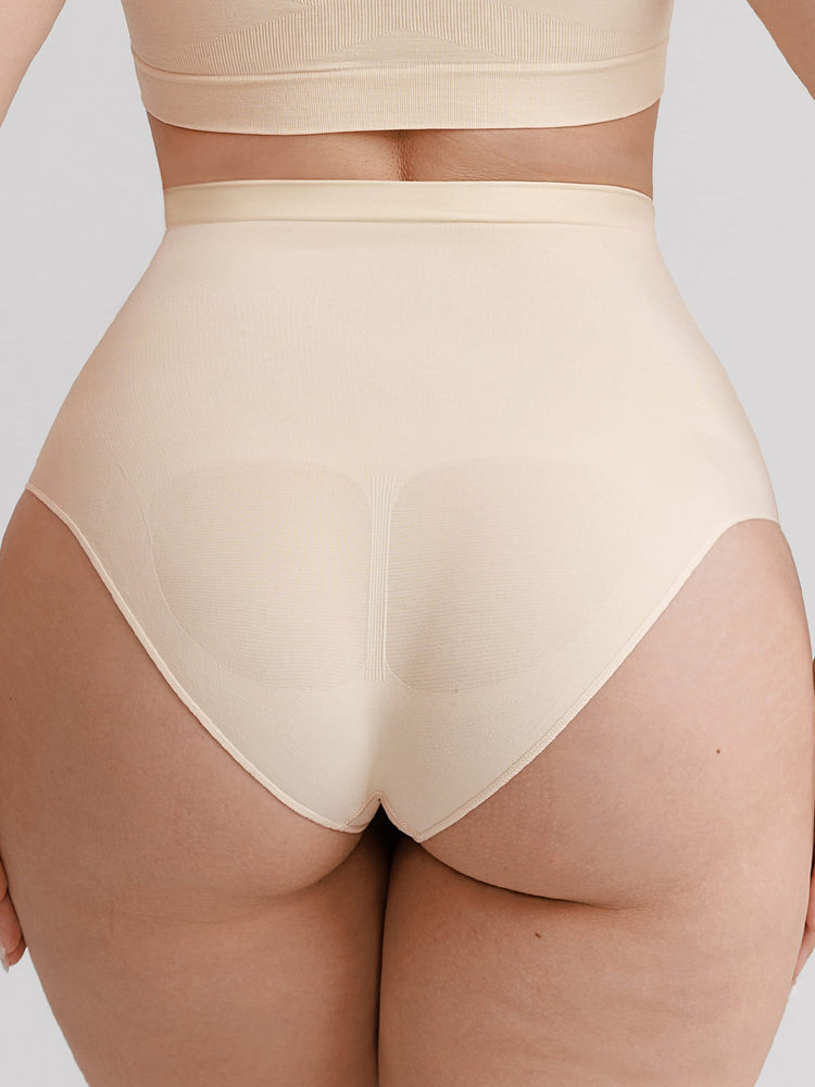 Rear view of a model wearing high-waisted shapewear briefs in a light beige/nude color, paired with a matching bandeau top against a solid gray background.